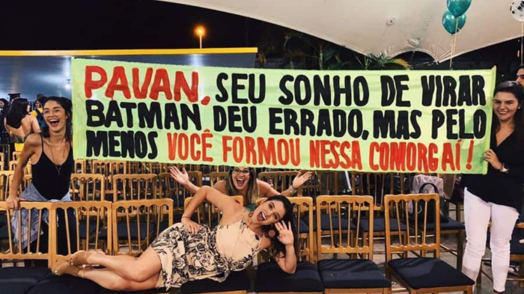 mulher deitada em 4 cadeiras e 3 amigas segurando faixa de formatura em homenagem