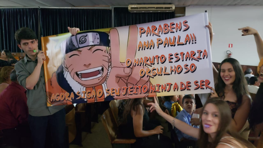 pessoas jovens segurando uma faixa de formatura com dizeres e a foto do anime naruto estampada