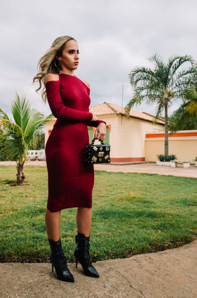 mulher de cabelo loiro vestida com vestido vermelho de ombro de fora com bota preta na altura da canela